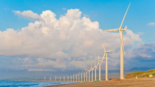 Wind turbines on beach against cloudy sky