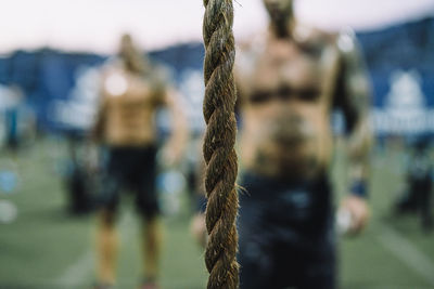 Close-up of rope in gym with shirtless men standing in background