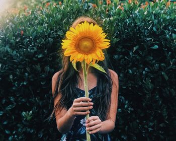 Teenage girl holding sunflower against plants