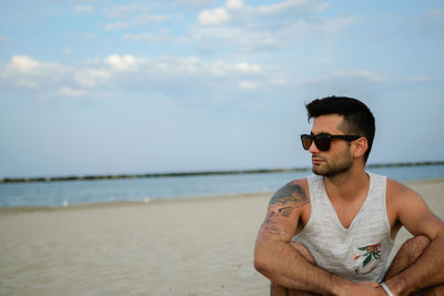 Young man wearing sunglasses at beach against sky