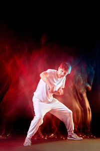 Side view of man with arms raised against black background