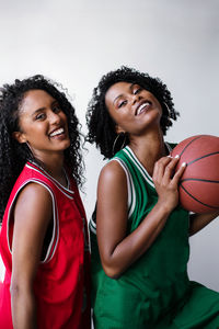 Two black women wearing basketball jerseys holding basketball on a white background