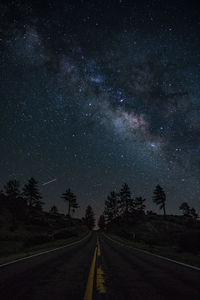 Road amidst trees against sky at night