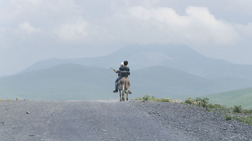 Friends riding donkey on road against sky