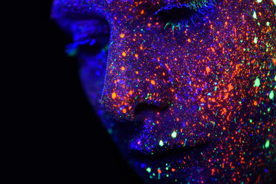 Close-up of woman with multi colored paint on face against black background