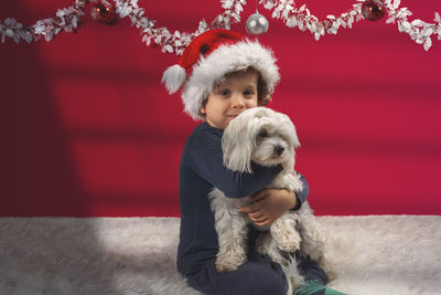 Cute little boy with christmas hat and decorations, hugging his little doggy