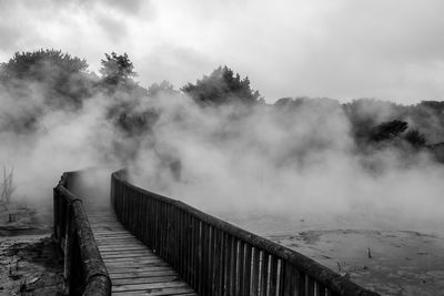Footbridge over river against foggy sky