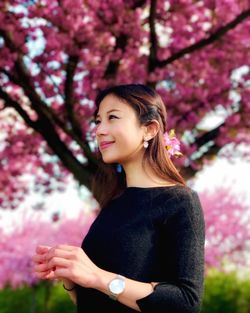 Young woman looking away while sitting on cherry tree in park