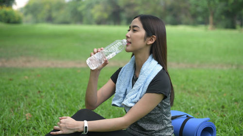 Side view of young woman drinking glass on field