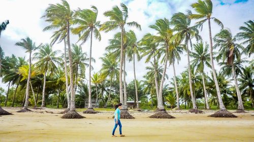 Side view of young woman walking on sand at beach against palm trees
