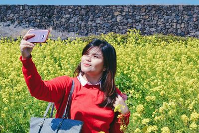 Young woman talking selfie through smart phone while standing at field during sunny day