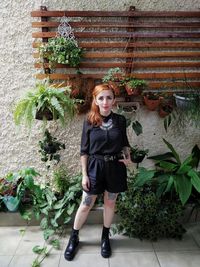Portrait of young woman standing against potted plants