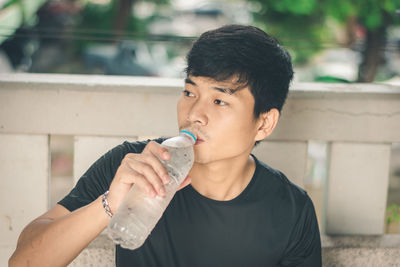 High angle view of young man drinking water while sitting on bench