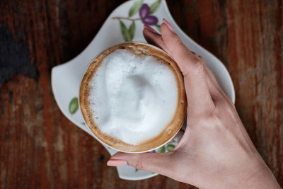 Close-up of hand holding coffee cup on table