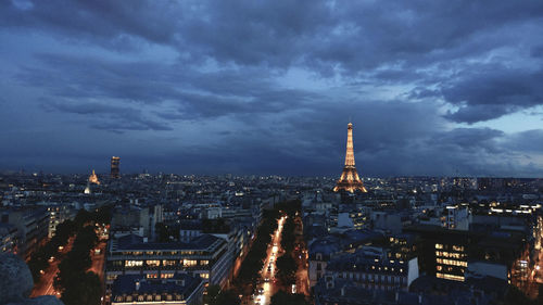 Illuminated buildings in city against cloudy sky