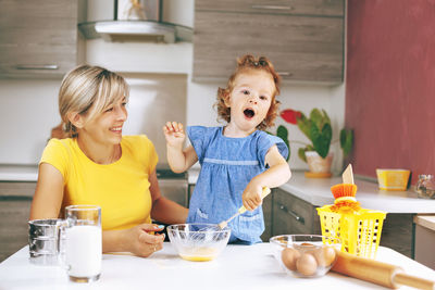 Smiling mother with daughter preparing food at kitchen