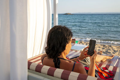 Middle-aged woman on vacation relax in daybed holding her smart phone chatting with and technology