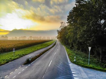 Empty road by trees on field against sky