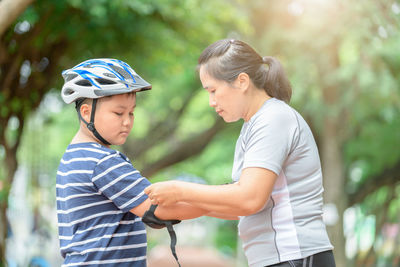 Mother assisting son in wearing elbow pad in park