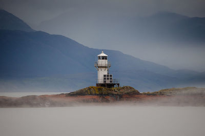 Lighthouse by building against sky