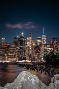 Illuminated buildings by river against sky at night