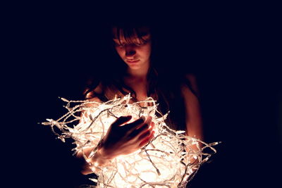 Close-up of teenage girl with illuminated string lights against black background