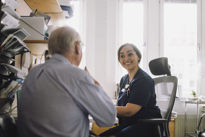 Happy female nurse listening to senior male patient during visit in clinic