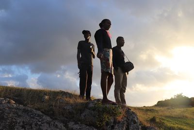 Friends standing on shore against sky during sunset