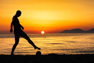 Silhouette man playing with ball at beach against sky during sunset