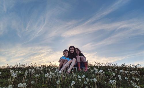 Low angle view of siblings sitting on grass against sky