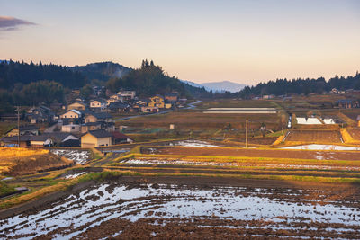 Scenic view of field by houses against sky during sunset