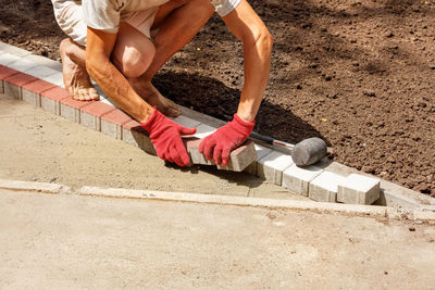 A worker lays paving slabs on a park path on a bright sunny day.