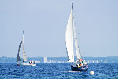 People sailing sailboats in sea against sky