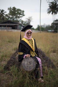 Portrait of woman in graduation gown sitting on log