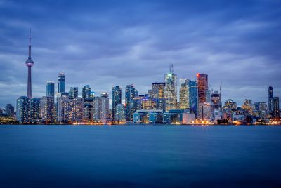 Illuminated buildings in city against cloudy sky