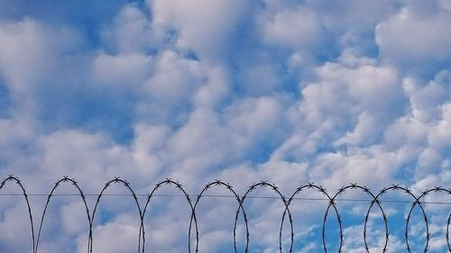Barbed wire fence against cloudy sky