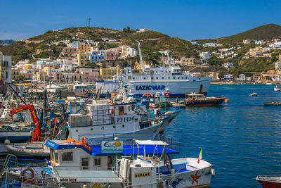 Sailboats moored on harbor by buildings against blue sky