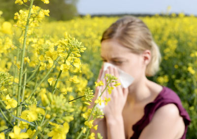 Woman cleaning nose by yellow flowering plants