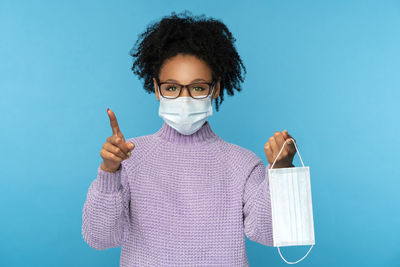 Portrait of young woman wearing mask against blue background