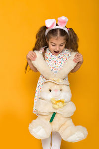 Portrait of cute girl with teddy bear against yellow background