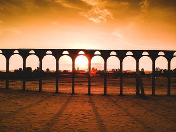 Silhouette bridge over sea against sky during sunset