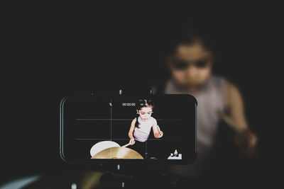 Close-up of mobile phone against girl playing musical instrument in background