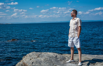 Woman standing on rock by sea against sky