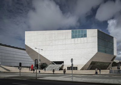 People walking by modern buildings in city against sky