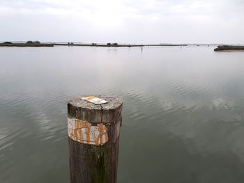 Wooden post in lake against sky