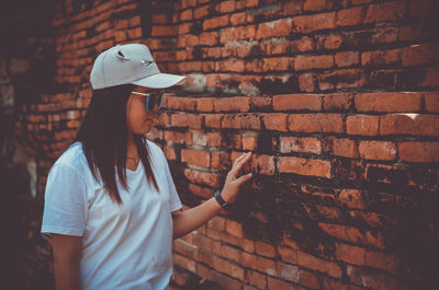 Woman wearing hat standing against brick wall