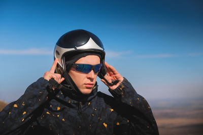 A young male paraglider in sunglasses fastens his helmet on a sunny day. preparing for paragliding