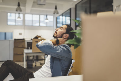 Side view of young businessman having neck ache while sitting in new office