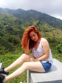 Beautiful young woman sitting on mountain against sky