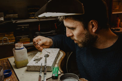 Male goldsmith using manual tool to shape metal ring in workshop